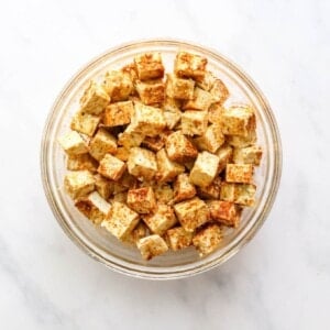 Cubes of seasoned tofu in a glass mixing bowl.