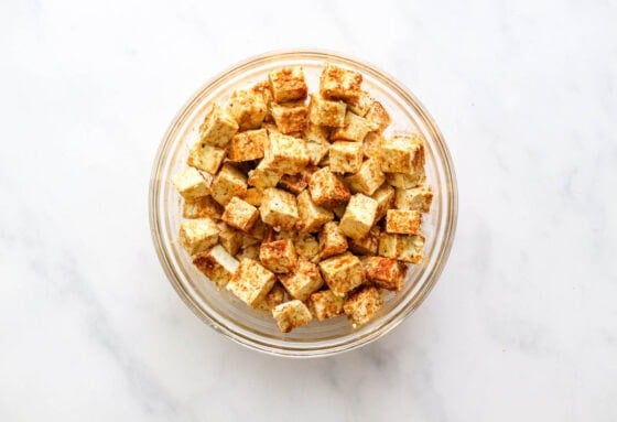 Cubes of seasoned tofu in a glass mixing bowl.