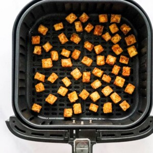 Cubes of seasoned air fryer tofu in an air fryer basket.