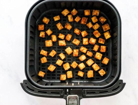 Cubes of seasoned air fryer tofu in an air fryer basket.