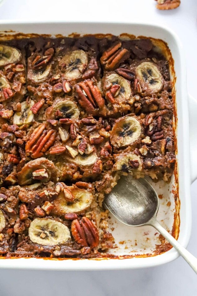 A baking dish containing baked steel cut oats topped with banana slices and pecans. A serving has been removed from the bottom corner.