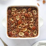 An overhead photo of an 8x8 baking dish with baked steel cut oats topped with banana slices and pecans.