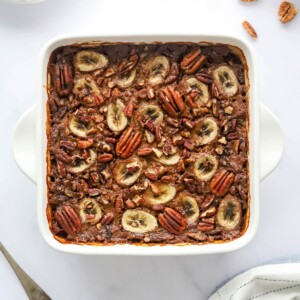 An overhead photo of an 8x8 baking dish with baked steel cut oats topped with banana slices and pecans.