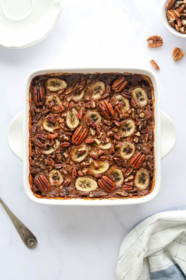 An overhead photo of an 8x8 baking dish with baked steel cut oats topped with banana slices and pecans.