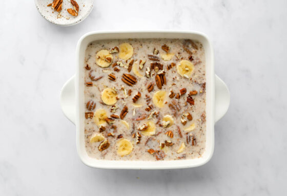 Steel cut oatmeal mixture poured into an 8x8 baking dish, topped with extra banana slices and pecans.