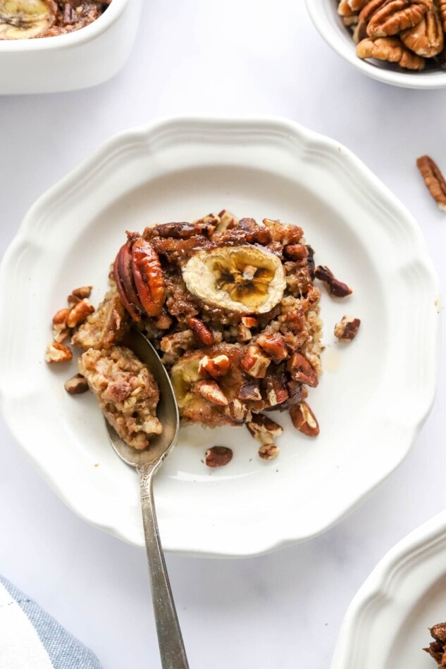 A serving of baked steel cut oats on a plate, drizzled with maple syrup. A spoon is removing a bite.