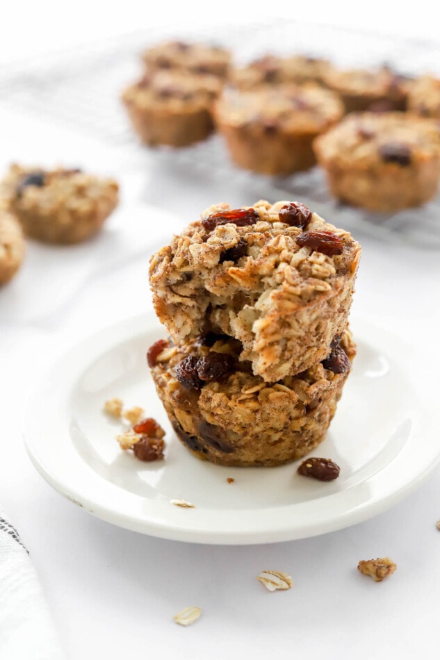 Two banana baked oatmeal cups stacked on a small plate. The top oatmeal cup has a bite taken out of it.