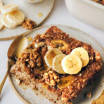 A serving of banana bread baked oatmeal on a plate topped with fresh banana slices and walnuts.