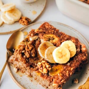A serving of banana bread baked oatmeal on a plate topped with fresh banana slices and walnuts.