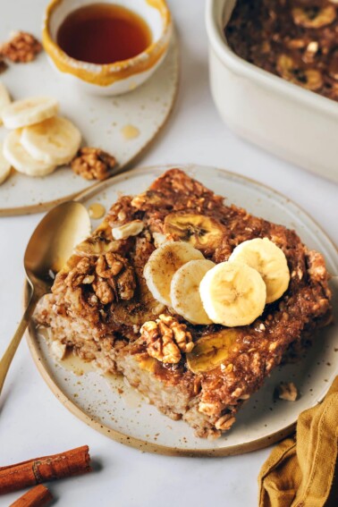 A serving of banana bread baked oatmeal on a plate topped with fresh banana slices and walnuts.