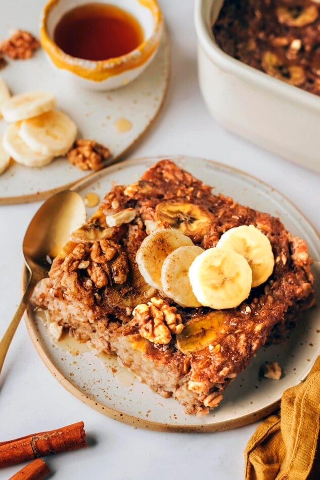 A serving of banana bread baked oatmeal on a plate topped with fresh banana slices and walnuts.