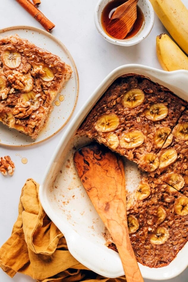 Banana Bread Baked Oatmeal in a baking dish. The oatmeal has been portioned in to 4 servings, with one serving removed from the baking dish and on a plate.