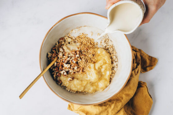 Milk, maple syrup, flaxseed, coconut oil, vanilla, mashed bananas and walnuts being added to the oat mixture.