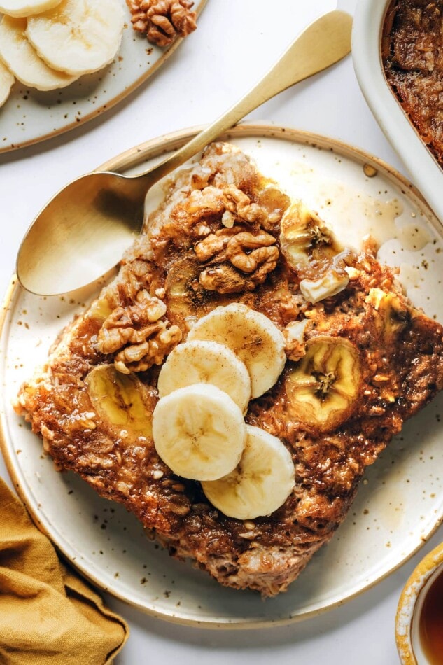 An overhead photo looking down on a plate with a serving of banana bread baked oatmeal topped with fresh banana slices. A spoon rests on the plate.