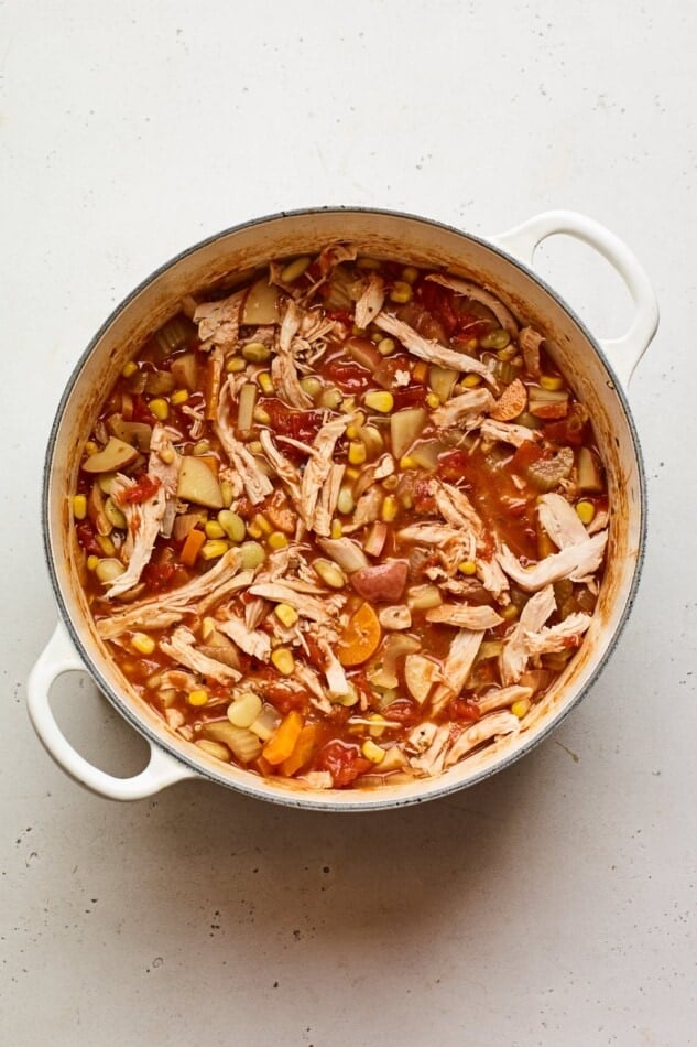 Shredded chicken added to a dutch oven containing Brunswick Stew.