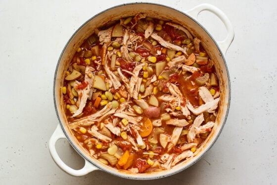 Shredded chicken added to a dutch oven containing Brunswick Stew.