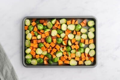 Seasoned sweet potato chunks and brussels sprouts halves spread around a baking sheet.