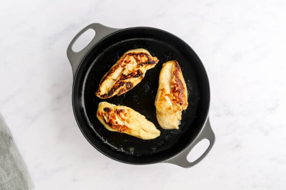 Three chicken breasts cooking in a skillet.