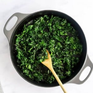 Wilting kale with a wooden spoon in a skillet.