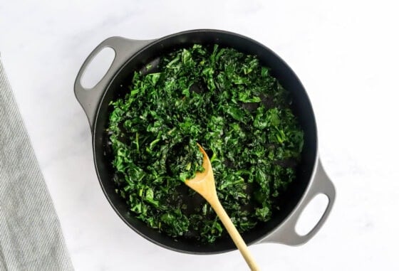 Wilting kale with a wooden spoon in a skillet.