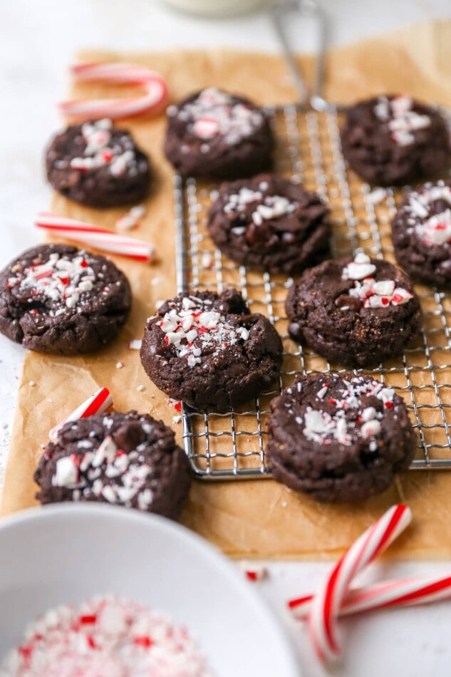 Chocolate peppermint cookies on a wire cooling rack and brown parchment paper. Candy cane pieces are scattered around.