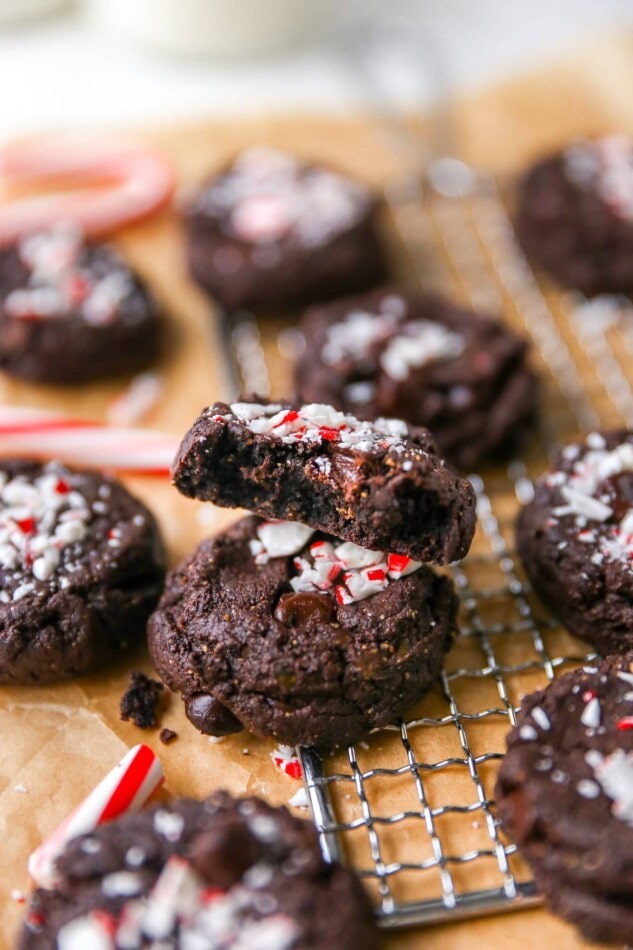 Chocolate peppermint cookies on a wire rack. A cookie with a bite taken out of it is stacked on top of another cookie in the center.
