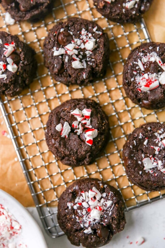 A close up overhead photo looking down at chocolate peppermint cookies on a wire cooling rack on top of brown parchment paper.