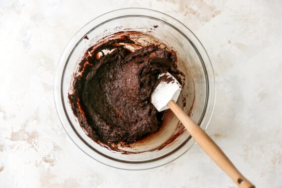 Chocolate peppermint cookie dough batter in a glass mixing bowl. A spatula rests in the bowl.