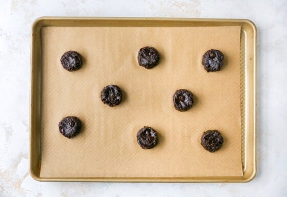 8 chocolate peppermint cookie dough balls on a parchment lined baking sheet.
