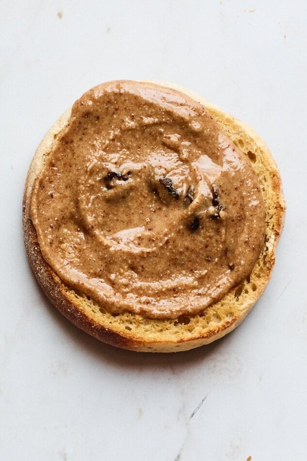 A toasted english muffin covered with cinnamon raisin almond butter.