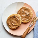 A plate with two halves of an english muffin, slathered with homemade cinnamon raisin almond butter.