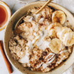 An overhead photo of a bowl of cinnamon raisin oatmeal topped with banana slices and a drizzle of coconut butter.