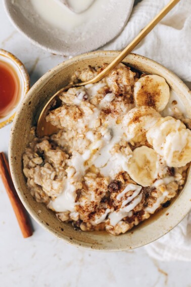 An overhead photo of a bowl of cinnamon raisin oatmeal topped with banana slices and a drizzle of coconut butter.