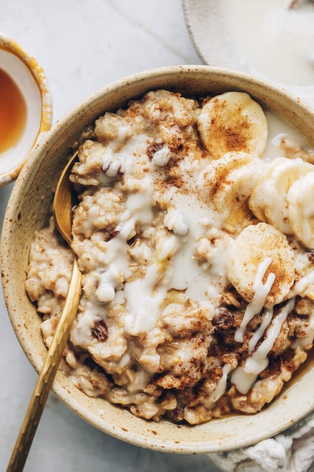An overhead and closeup photo of a bowl of cinnamon raisin oatmeal topped with banana slices and a drizzle of coconut butter.