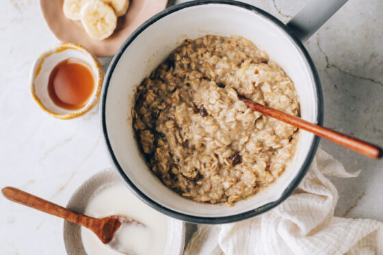 Cooked cinnamon raisin oatmeal in a pot. A wooden spoon rests in the pot.