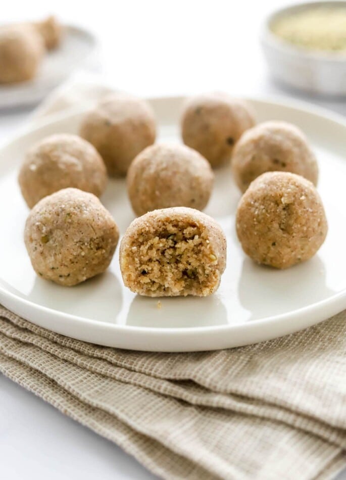 Eight coconut protein balls on a plate, the front and center ball has a bite taken out of it, exposing the inside.