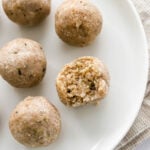 An overhead photo looking down at 5 coconut protein balls on a plate. One of the balls has a bite taken out of it.