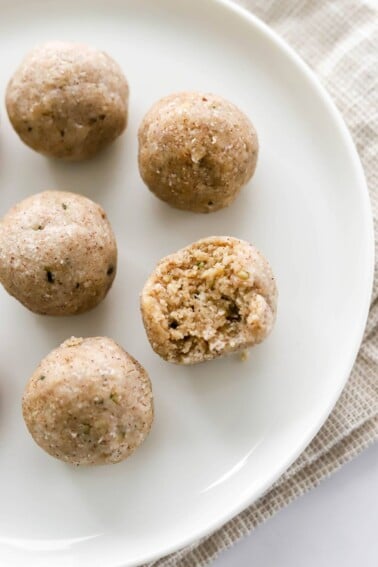 An overhead photo looking down at 5 coconut protein balls on a plate. One of the balls has a bite taken out of it.