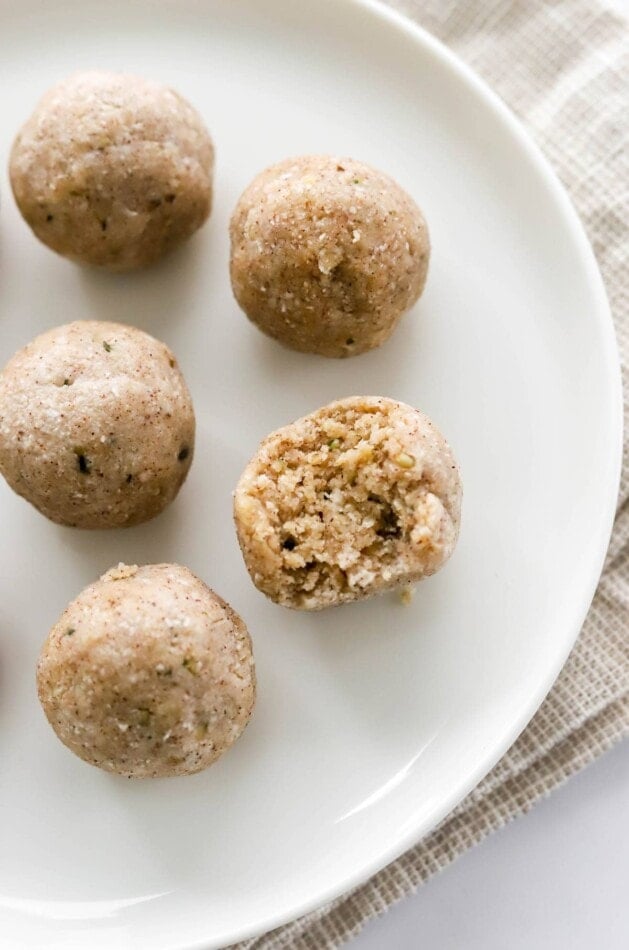 An overhead photo looking down at 5 coconut protein balls on a plate. One of the balls has a bite taken out of it.