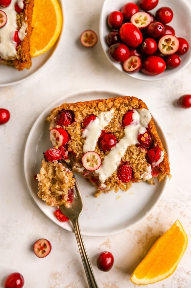An overhead photo looking at a slice of cranberry orange baked oatmeal on a plate. A fork has a bite ready next to the slice.