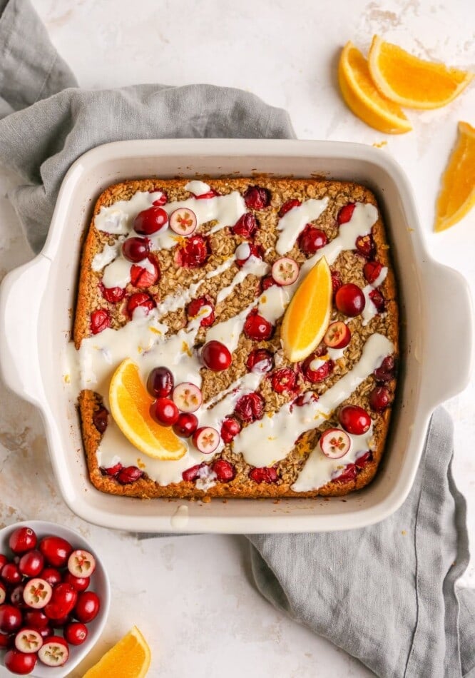 An overhead photo of a baking dish with cranberry orange baked oatmeal topped with a maple orange glaze, orange slices and whole cranberries.