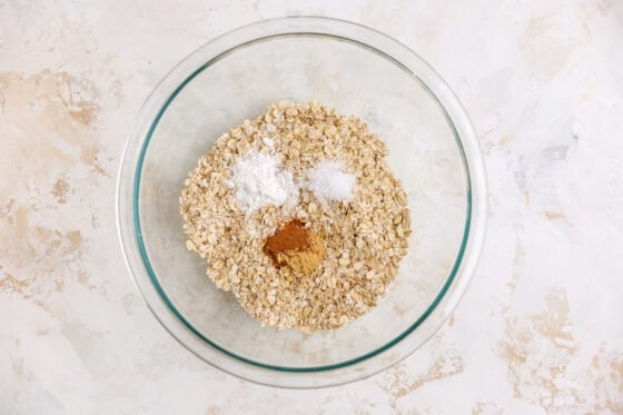 A mixing bowl containing oats, baking powder, cinnamon, ginger and salt.