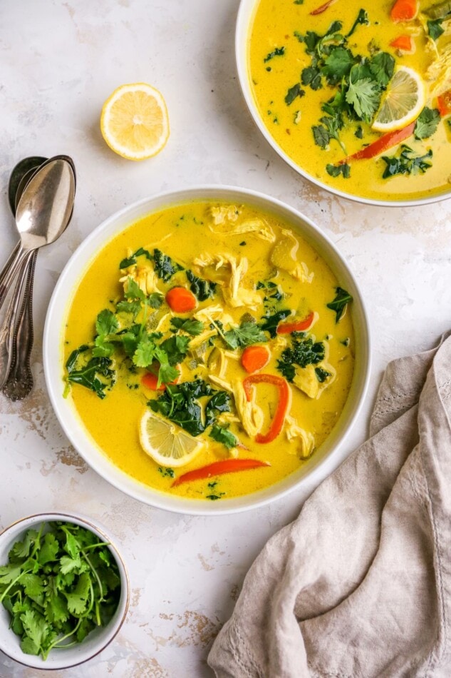 Two bowls of detox soup. There are two spoons nearby and a small dish of fresh cilantro.