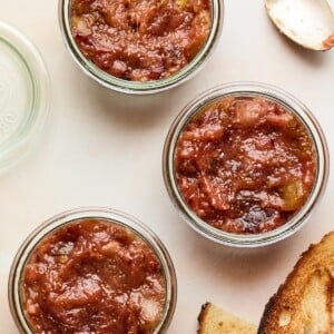 An overhead photo looking down at 3 jars of homemade fig jam. A spoon and two slices of toasted bread are next to the jars.