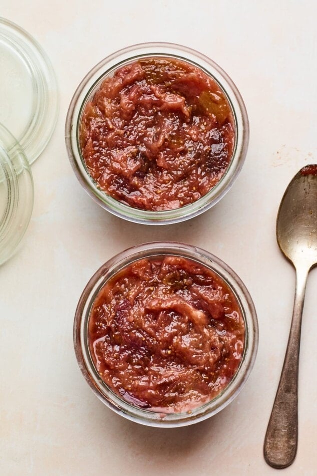 An overhead photo looking down at two small jars of homemade fig jam. A metal spoon is laying next to the jars.