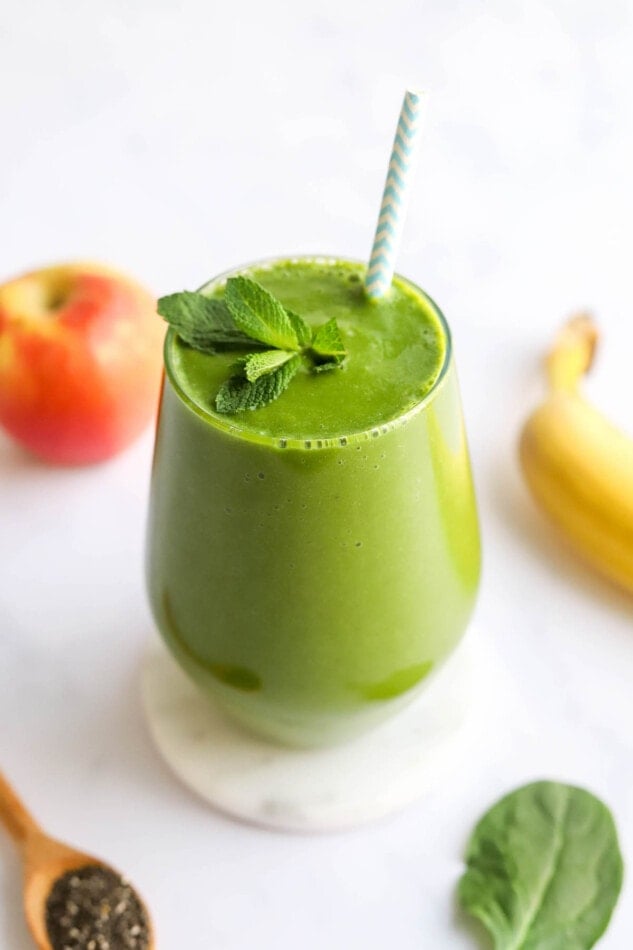 A glass containing green detox smoothie, topped with a fresh sprig of mint and with a striped straw.