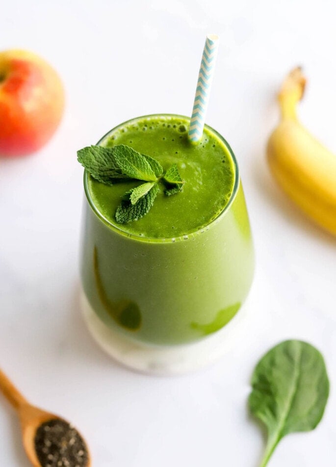 A glass containing green detox smoothie topped with a sprig of fresh mint and a striped straw.