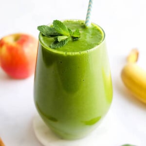 A glass containing green detox smoothie topped with a sprig of fresh mint and a striped straw.