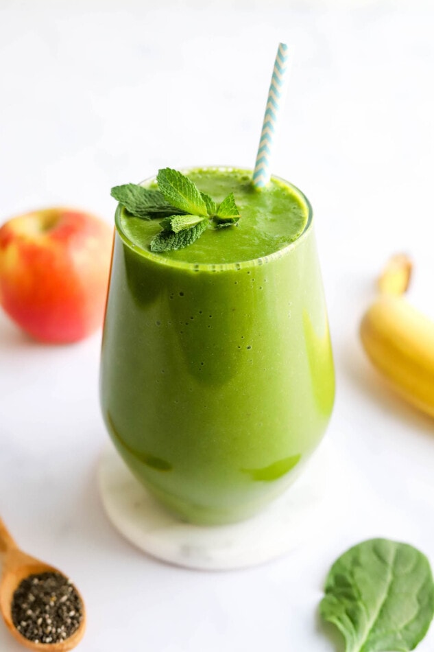 A glass containing green detox smoothie topped with a sprig of fresh mint and a striped straw.