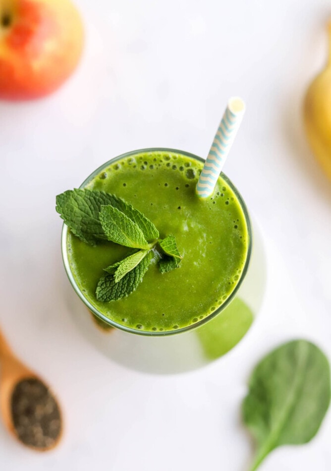 An overhead view of a glass containing green detox smoothie topped with a sprig of fresh mint and a striped straw.